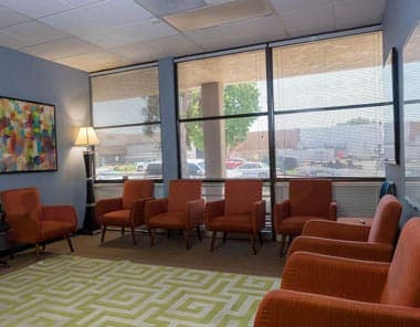 Orange chairs line a group room with a window wall and a patterned rug.